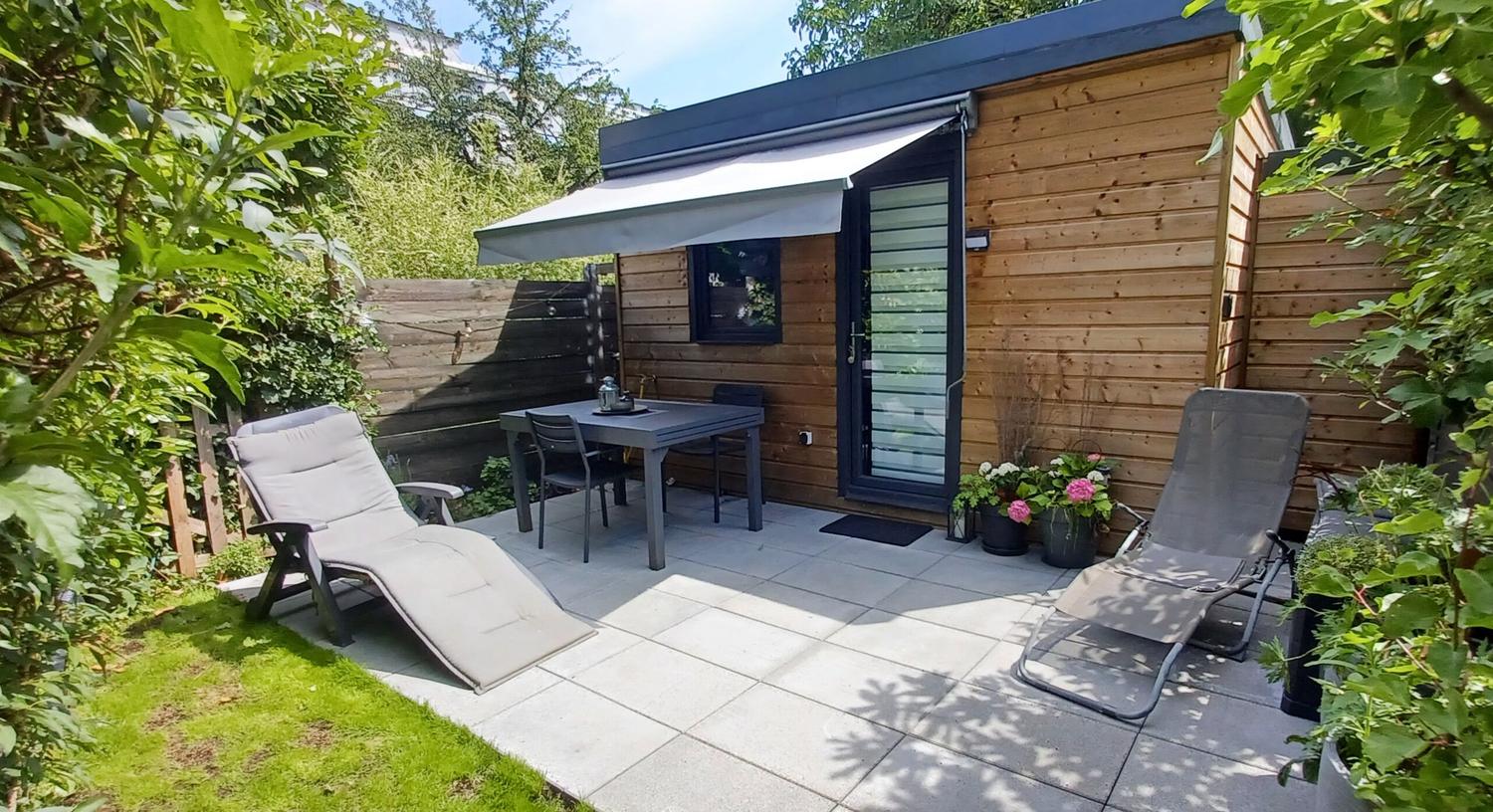 La terrasse dallée avec store, table et chaises longues devant le studio